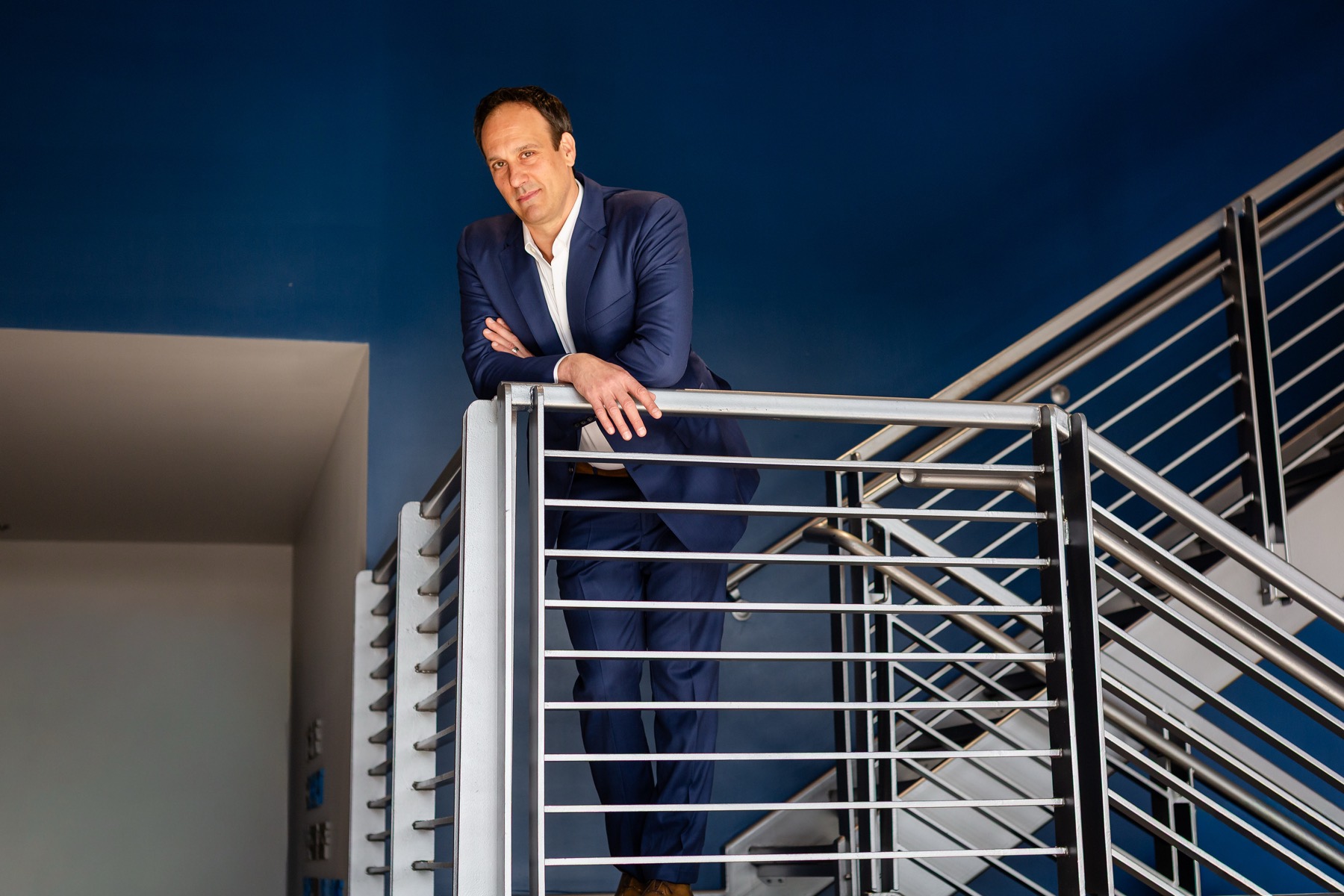Michael Bernoff leaning on a stair railing in a blue suit