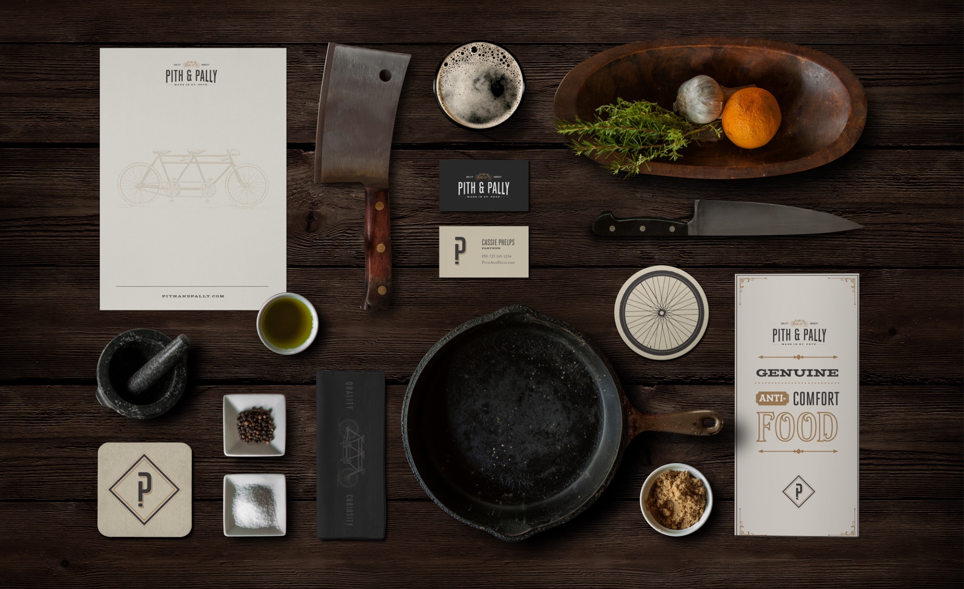 Pith & Pally stationery, business cards, coasters and menu laid out on a dark wood table with kitchen tools