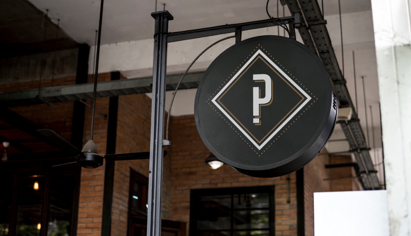 Round Pith & Pally blade sign with the P monogram hanging outside a brick building