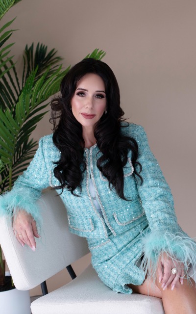 Sara Wolfe in a turquoise jacket seated in a white chair