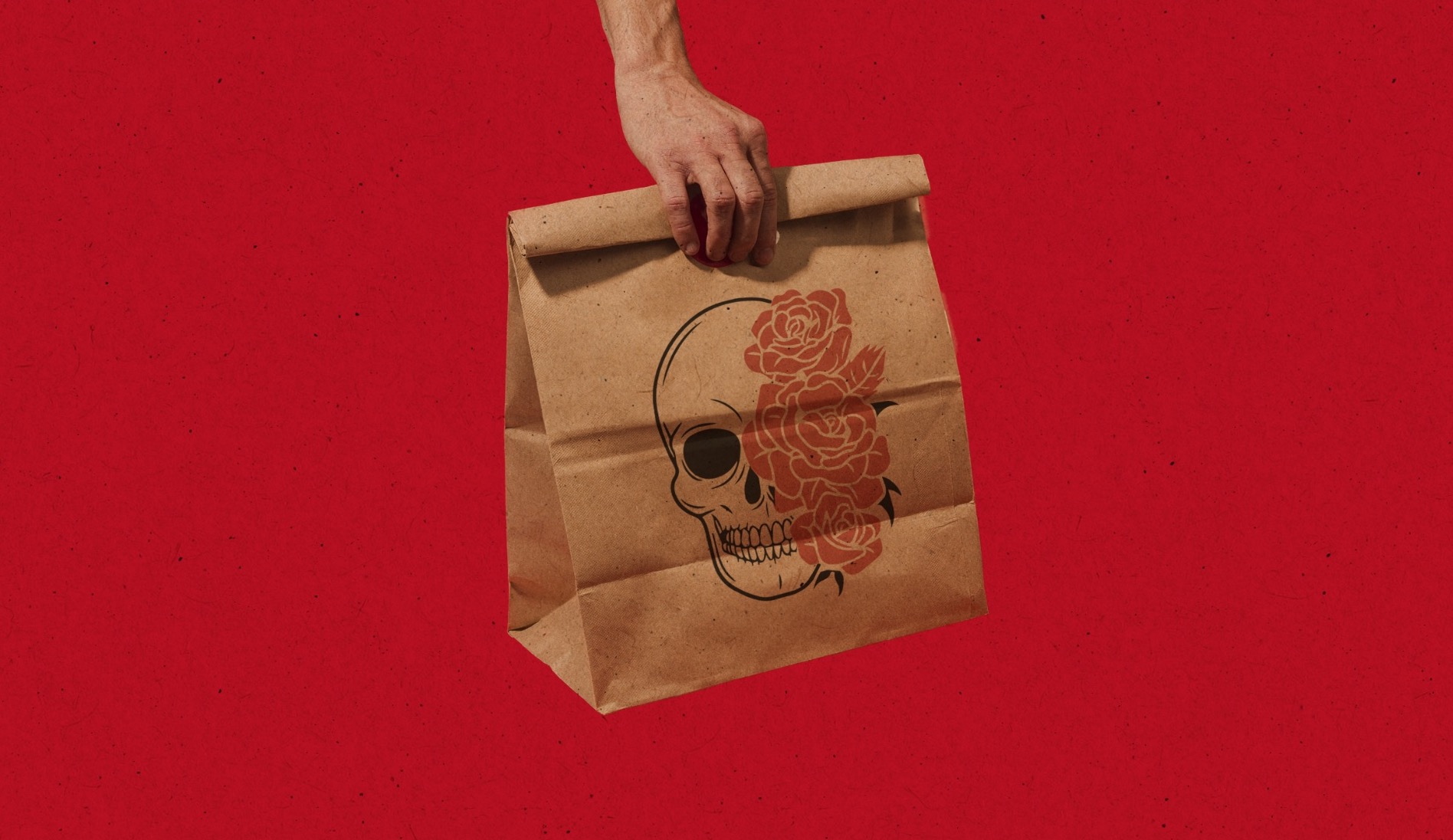 A hand carrying a kraft Taco Saint bag printed with the skull and roses