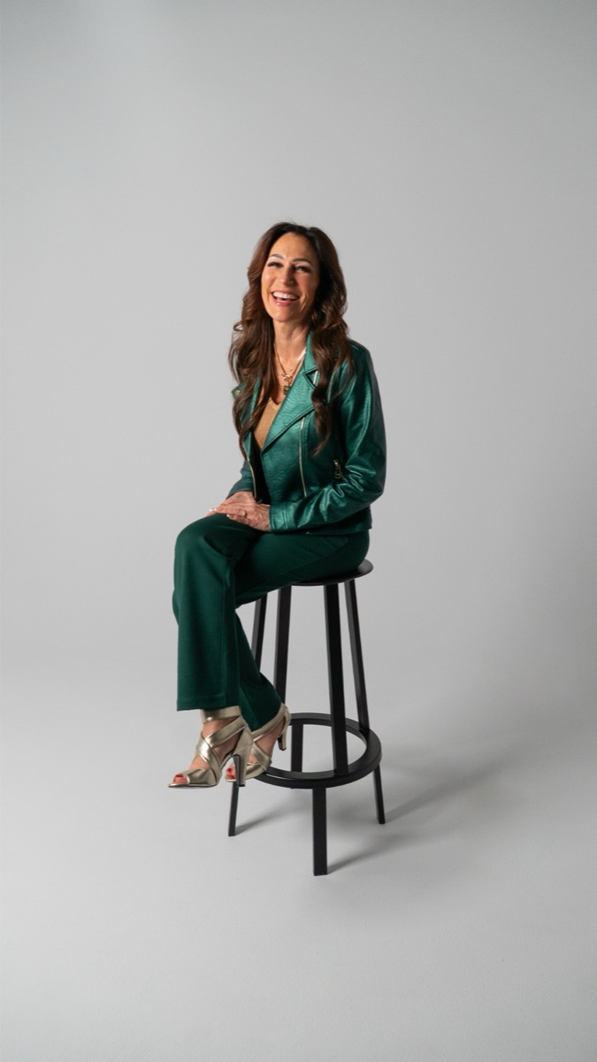 Tina Schaaf in an emerald suit on a tall stool